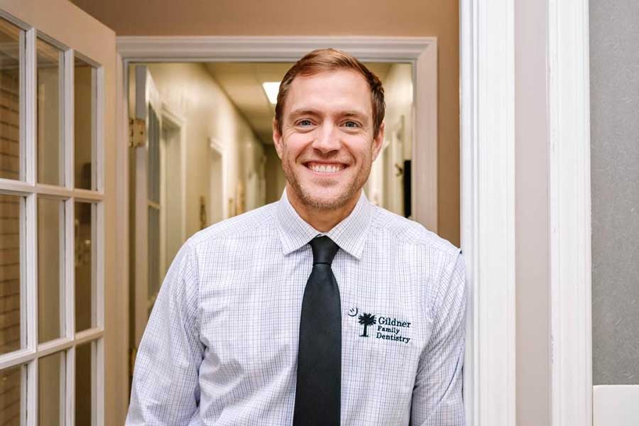 Dr. Robert Gildner, wearing a white shirt and black tie, standing in the doorway at Gildner Family Dentistry in Lexington, SC